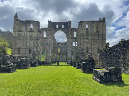 A stone building with arches and a green lawn
Description automatically generated